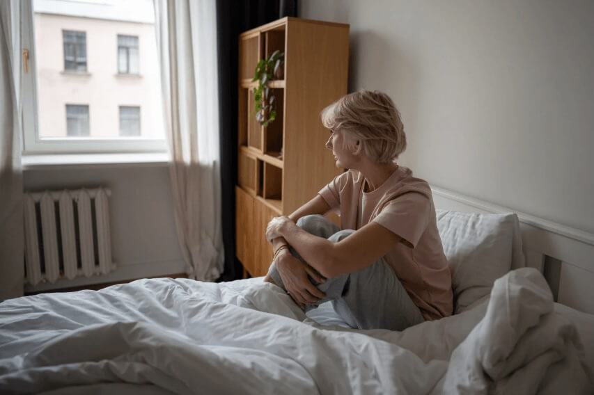Fatigued exhausted woman sitting in bed blankly staring at a window