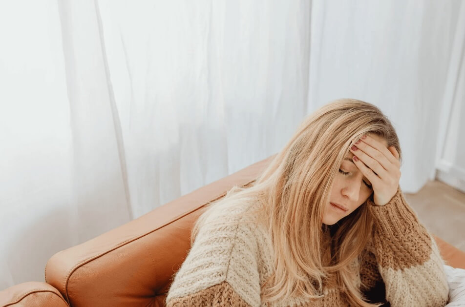 Woman sitting on a couch with eyes closed and putting her hand on her forehead